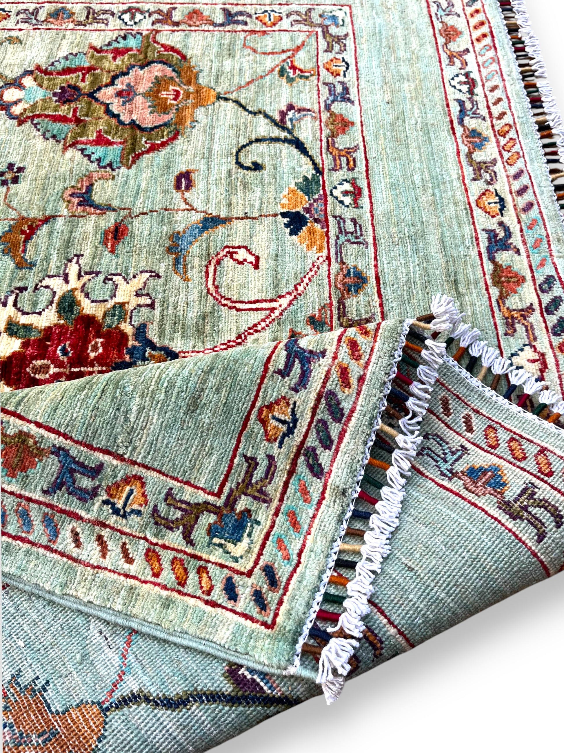 Corner detail of Afghan hand-knotted rug displaying traditional border patterns, cotton fringes, and precise weaving craftsmanship