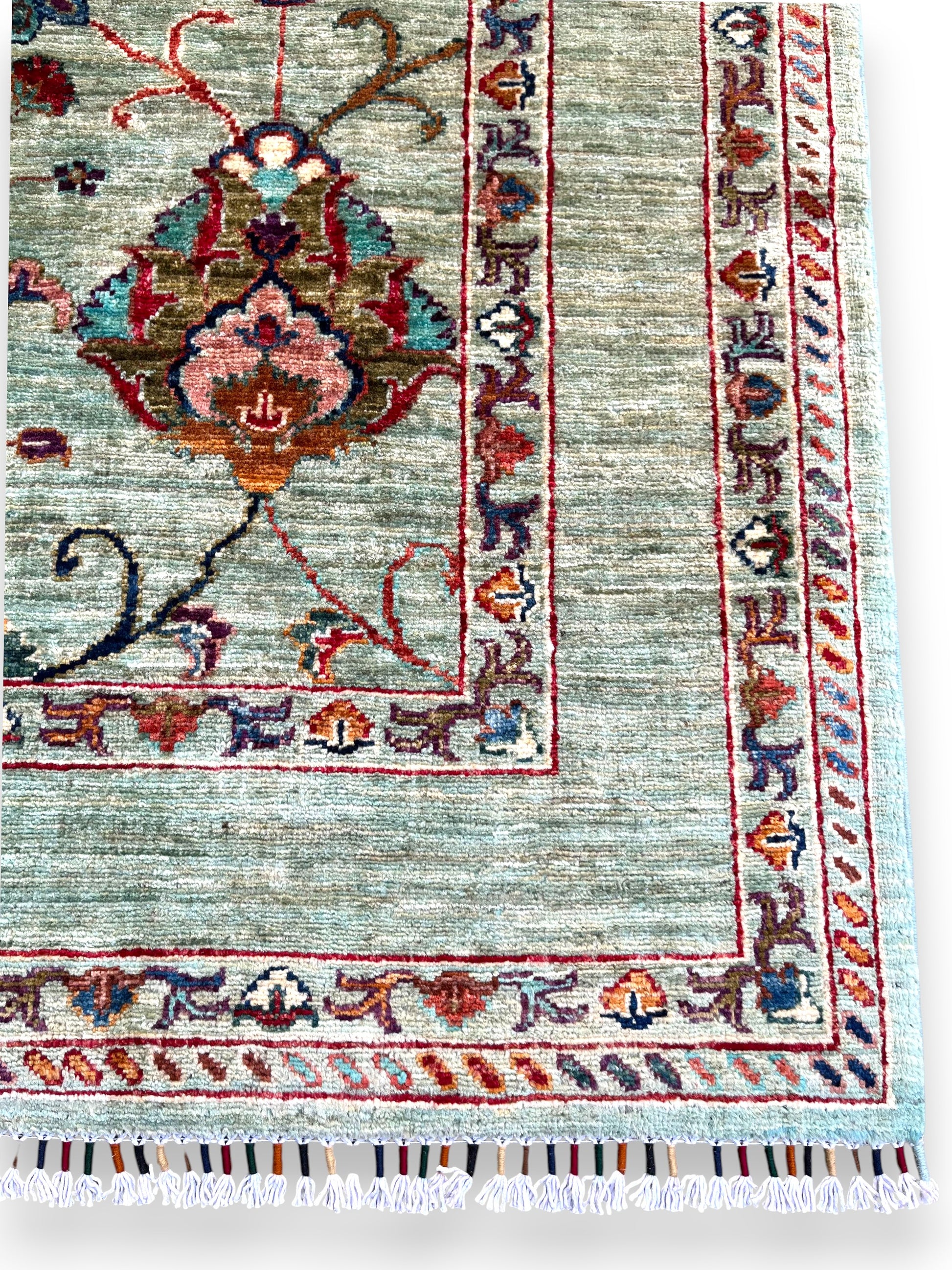 Close-up detail of Afghan rug showing intricate hand-knotted floral medallions in burgundy and coral with delicate vine scrollwork on sage green background