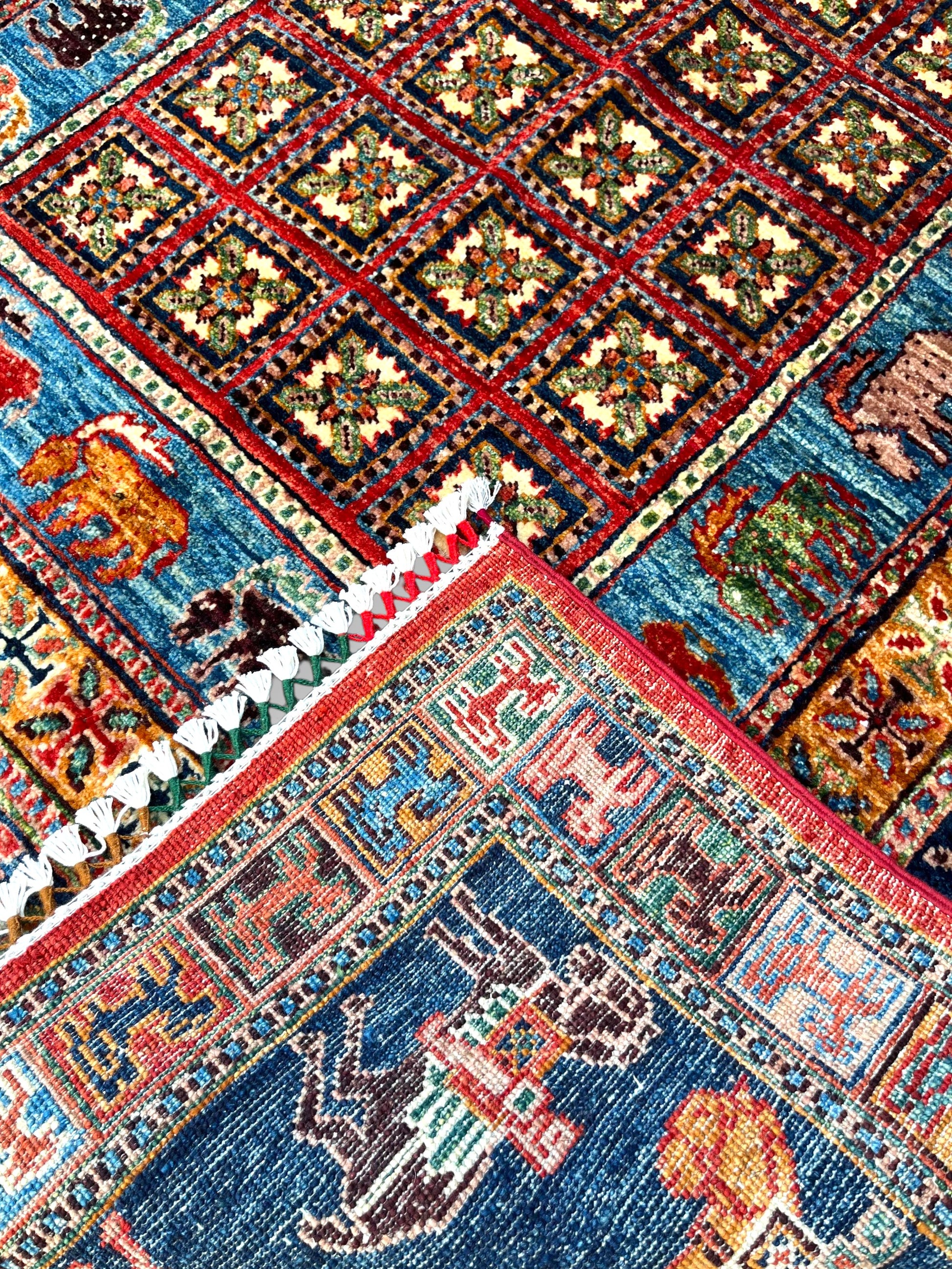 Detail view of navy blue border on Afghan pictorial rug featuring colorful horses, riders, and traditional animal motifs with turquoise and coral accents