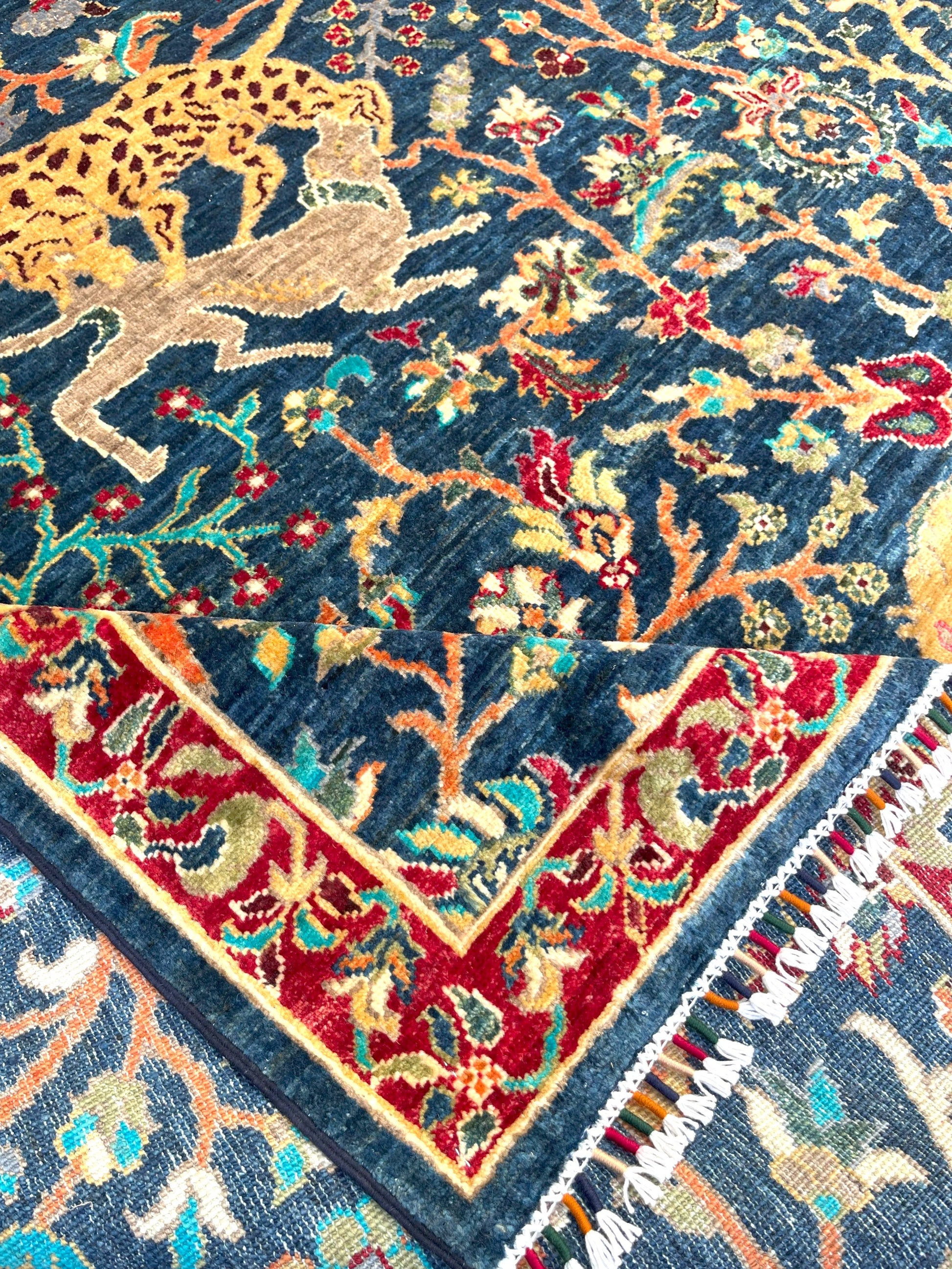 Close-up detail of Afghan wildlife rug showing golden lions, deer, and ornate botanical motifs on navy wool field with intricate hand-knotted craftsmanship