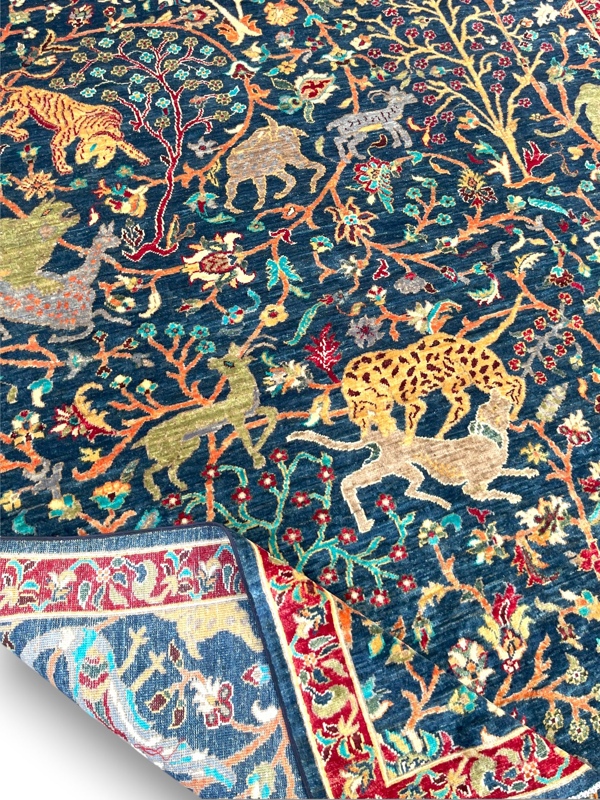 Detail view of red burgundy border on Afghan wildlife rug showing traditional palmette patterns and scrolling motifs with white cotton fringe
